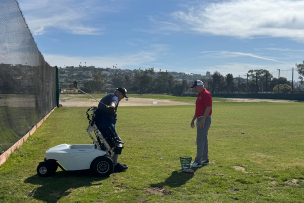 Athlete with a physical disability uses an adaptive golf cart while practicing a swing with a coach during a CAF adaptive golf clinic.
