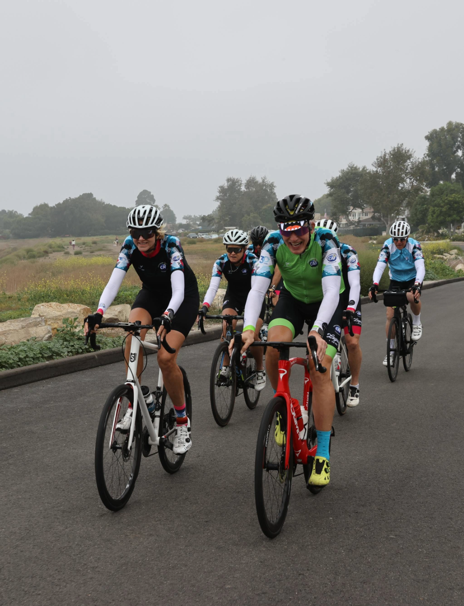 Group of cyclists riding together on a paved road, smiling during a group ride.