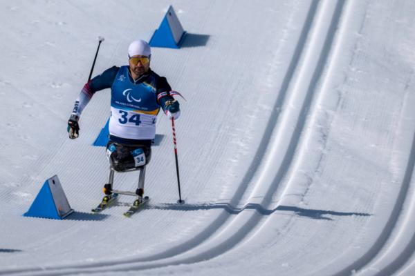 Athlete with a physical disability using a sit-ski competing in cross-country skiing, propelling forward with poles on a groomed snowy course during the Milano Cortina 2026 Winter Paralympics.
