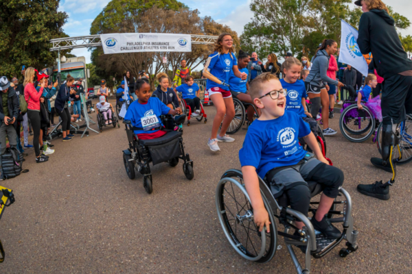 Brantley Volpel, a young athlete with spina bifida, raises his arms in celebration while being pushed in his wheelchair across the finish area at a Challenged Athletes Foundation Kids Run event.