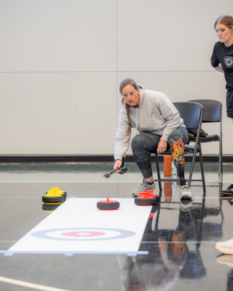A woman kneels on a sports court beside a curling target with stones.