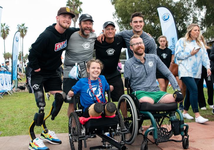 Group of CAF athletes with physical disabilities and supporters gather closely, smiling for a photo at an outdoor event.