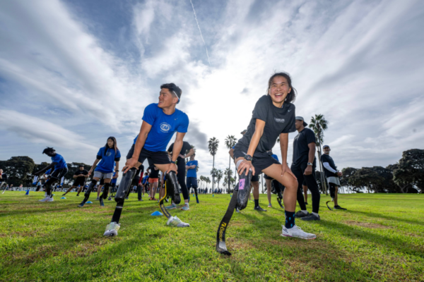 Athletes with physical disabilities stretch and prepare for a workout together on a grassy field during a CAF clinic.