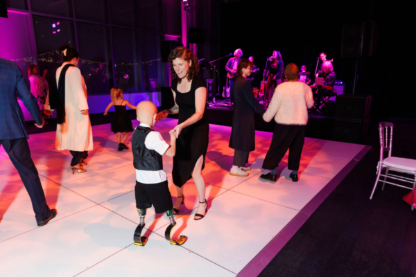 Guests dance on a white dance floor during the gala after-party while a live band performs on stage in the background under purple lighting.