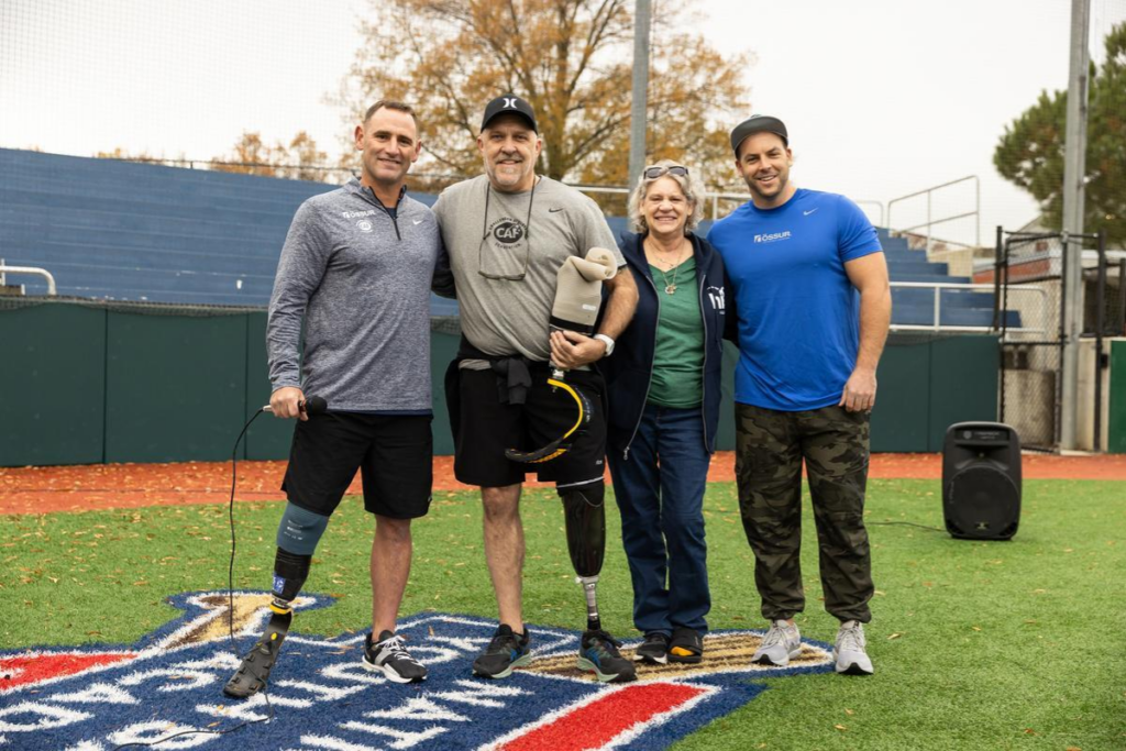 Four people standing together on a field, two using lower-limb prostheses.
