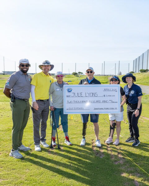 Group of six people on a golf course holding a large check made out to Julie Lyons.
