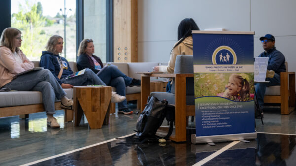 People sitting in a circle in a modern room with a banner for "Idaho Parents Unlimited, Inc."
