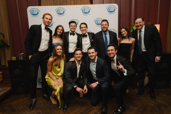 Group of attendees in formal attire pose together in front of a CAF step-and-repeat backdrop at an event
