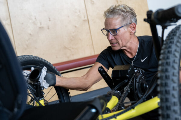 Person working on the wheel of a handcycle with a yellow frame indoors.