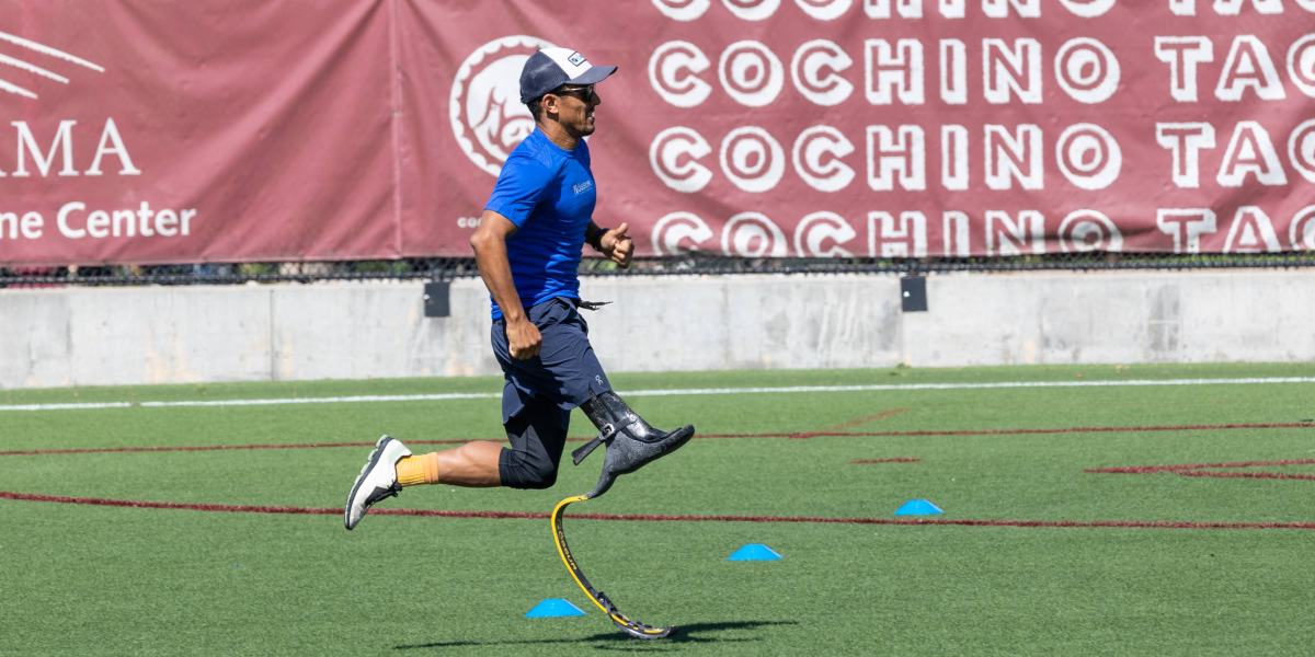 Athlete with a running prosthesis sprints across a training field, moving between cones during a speed drill.