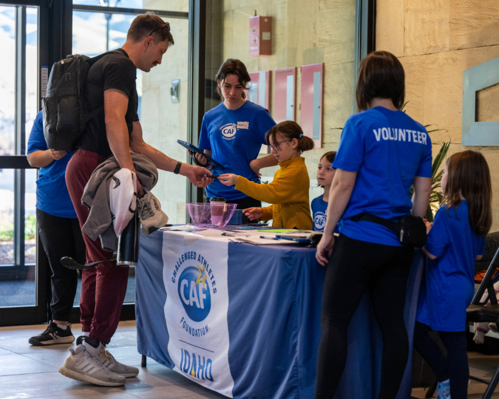 Participants, volunteers, and families gather at a CAF Idaho Symposium registration table as attendees check in at the event.