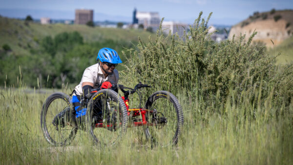 Person with a blue helmet riding an adaptive mountain bike through a grassy field.