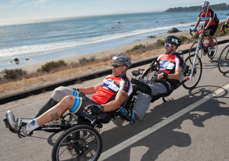 Adaptive cyclists ride handcycles and road bikes along a coastal roadway during a Challenged Athletes Foundation cycling event.