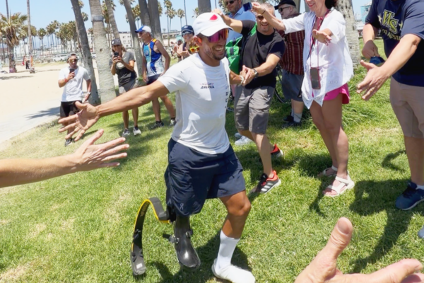 Adaptive athlete Mohamed Lahna greets supporters and volunteers after finishing Triathlon Across America on a prosthetic running leg.