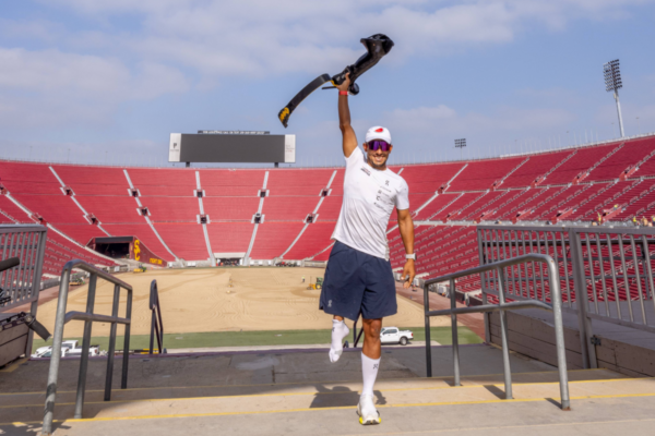 Adaptive athlete Mohamed Lahna raises a prosthetic leg inside a stadium as part of the Triathlon Across America endurance challenge.