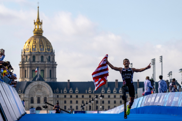Paralympic triathlete crossing the finish line with a United States flag at the Paris 2024 Paralympic Games.