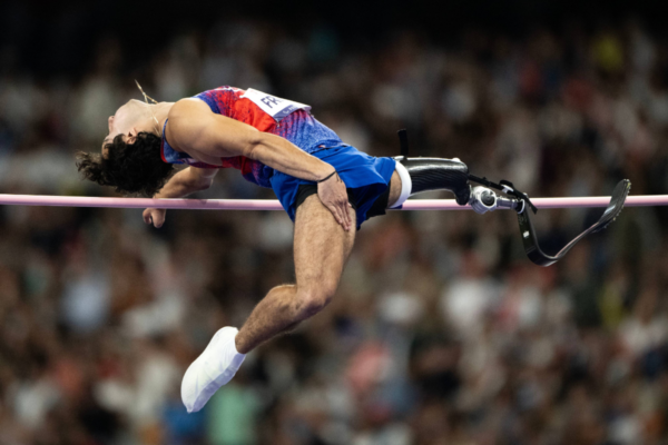 Paralympic high jump athlete using a prosthetic leg while clearing the bar during competition.