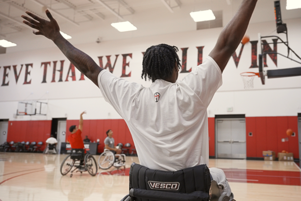 Wheelchair basketball participant raises both arms while practicing on an indoor basketball court during an adaptive sports clinic hosted by the Challenged Athletes Foundation.