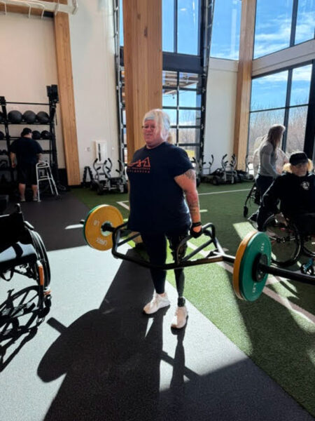 A person with a lower limb prosthesis lifting in a gym setting.