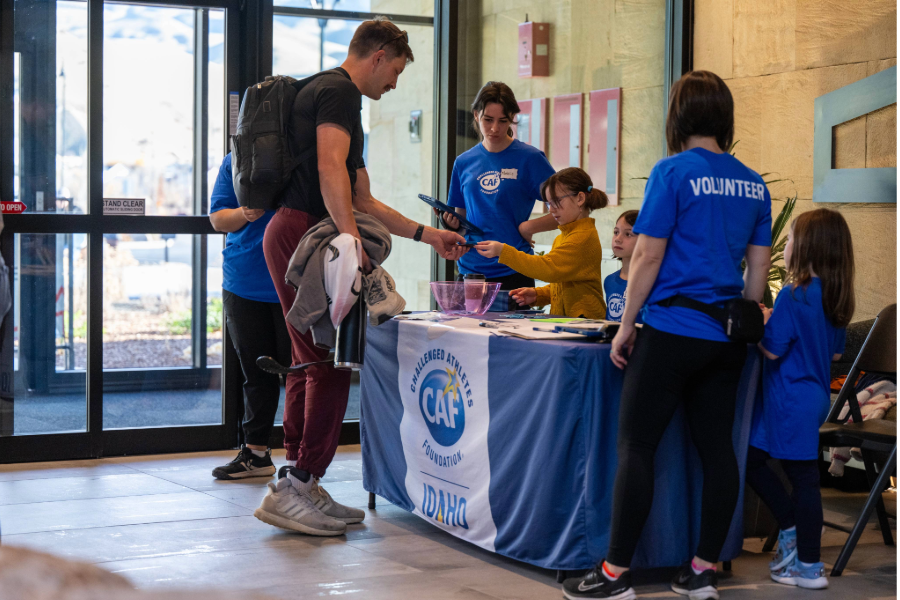 Participants, volunteers, and families gather at a CAF Idaho Symposium registration table as attendees check in at the event.