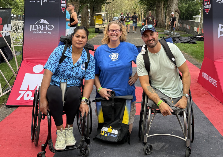 Two wheelchair athletes and a Challenged Athletes Foundation staff member pose beneath the IRONMAN 70.3 Boise finish arch on race weekend in Boise, Idaho.