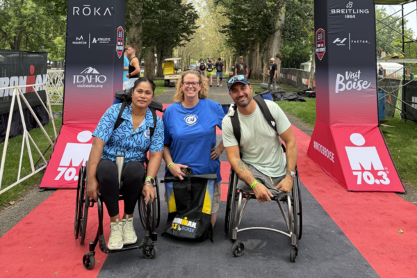 Two wheelchair athletes and a Challenged Athletes Foundation staff member pose beneath the IRONMAN 70.3 Boise finish arch on race weekend in Boise, Idaho.