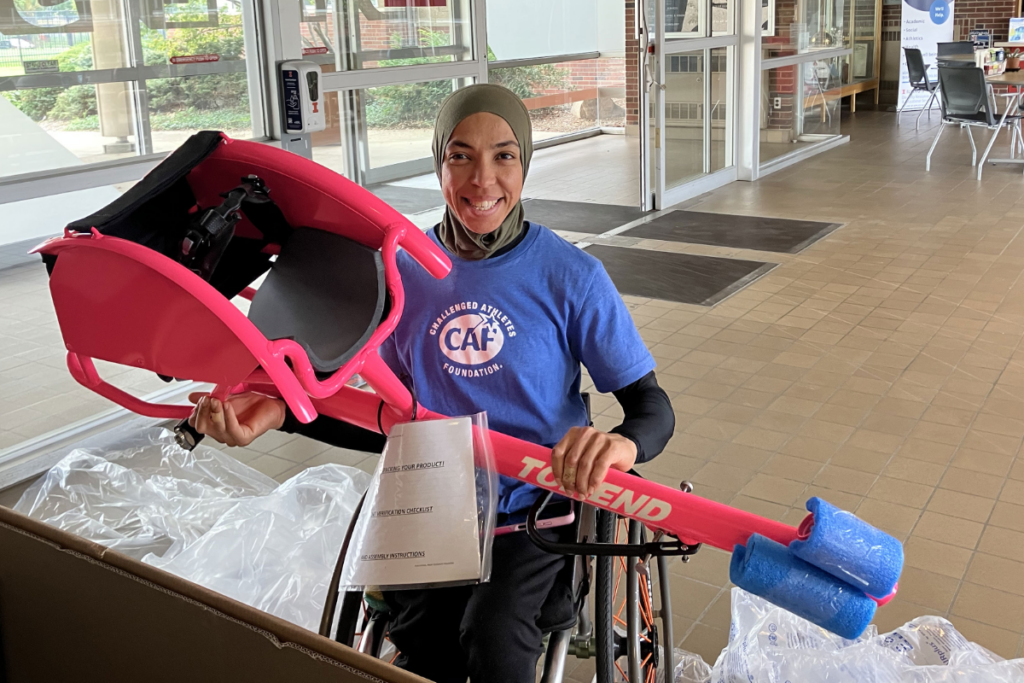 Hoda Mohammed smiling while holding the frame of a new pink adaptive sports wheelchair.
