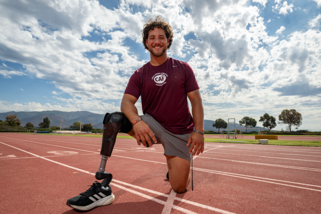 Parker Byrd kneeling on a running track wearing a running prosthesis and CAF shirt.