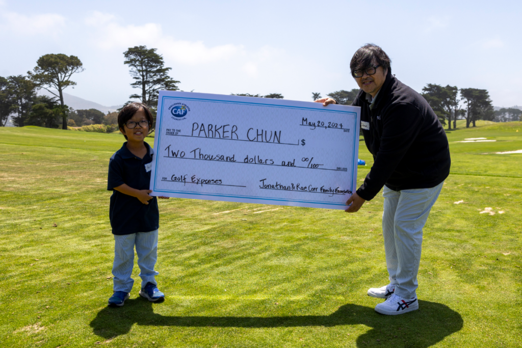 Parker Chun holding a $2,000 CAF grant check for golf expenses with a supporter on a golf course.