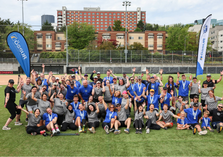 Adaptive athletes, coaches, volunteers, and clinic participants gather for a group photo on a sports field during a Challenged Athletes Foundation and Össur adaptive running clinic in Seattle.