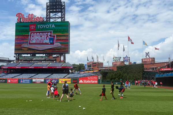 Participants practice baseball skills on the outfield grass at Citizens Bank Park beneath the Toyota Phillies Coaches Clinic scoreboard.