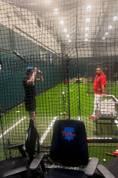 A youth participant practices batting inside the indoor training facility while a Philadelphia Phillies coach provides instruction during the Toyota Phillies Coaches Clinic.