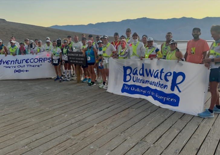 Badwater Ultramarathon runners and support crews gather at Badwater Basin in Death Valley before the start of the race, holding event banners at the lowest point in North America.