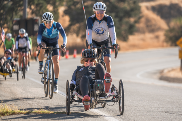 An athlete riding a recumbent handcycle travels on a roadway while cyclists ride behind during a CAF cycling event.