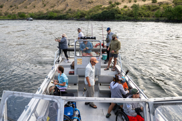 People fishing from an accessible boat on a wide river bordered by dry hills.