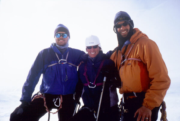 Three mountaineers in winter gear pose together in a snowy landscape.