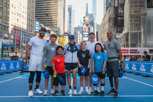 Adaptive athletes, youth participants, and instructors pose together on a CityPickle court following a pickleball clinic in Times Square, New York City.