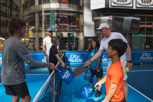 Participants and instructors exchange paddle taps across the net during a Challenged Athletes Foundation adaptive pickleball clinic at CityPickle in Times Square.