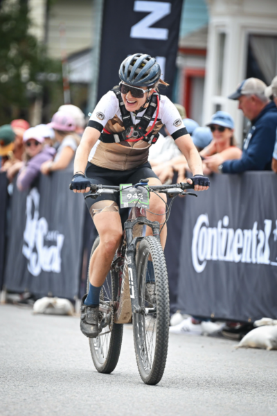 Adaptive mountain biker rides through the finish chute at the Leadville Trail 100 MTB, with spectators and race banners visible along the course.