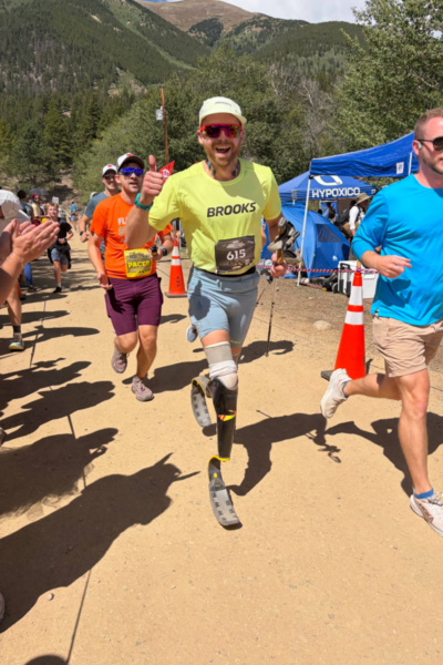 Athlete with a running prosthesis competes in the Leadville Trail 100 Run, passing aid station tents and spectators along the course.