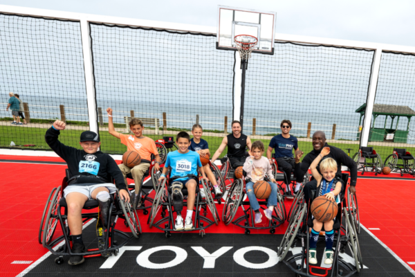 Wide view of athletes and participants seated on a Toyota-branded adaptive sport court during CAF Community Weekend, with adaptive sports equipment, wheelchairs, and a bayfront setting in the background.