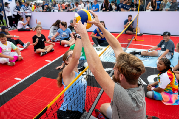 Youth and adult participants gather on a Toyota-branded adaptive basketball court, with several athletes in sport wheelchairs holding basketballs during an adaptive sports activity near the coastline.