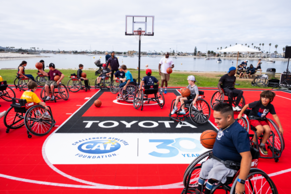Athletes in sport wheelchairs participate in an adaptive basketball clinic on a Toyota-branded court during a CAF event, with coaches and participants spread across the playing surface.