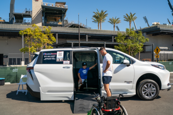 A participant exits an accessible Toyota mobility van using a wheelchair ramp while another participant stands nearby at an outdoor CAF event venue.