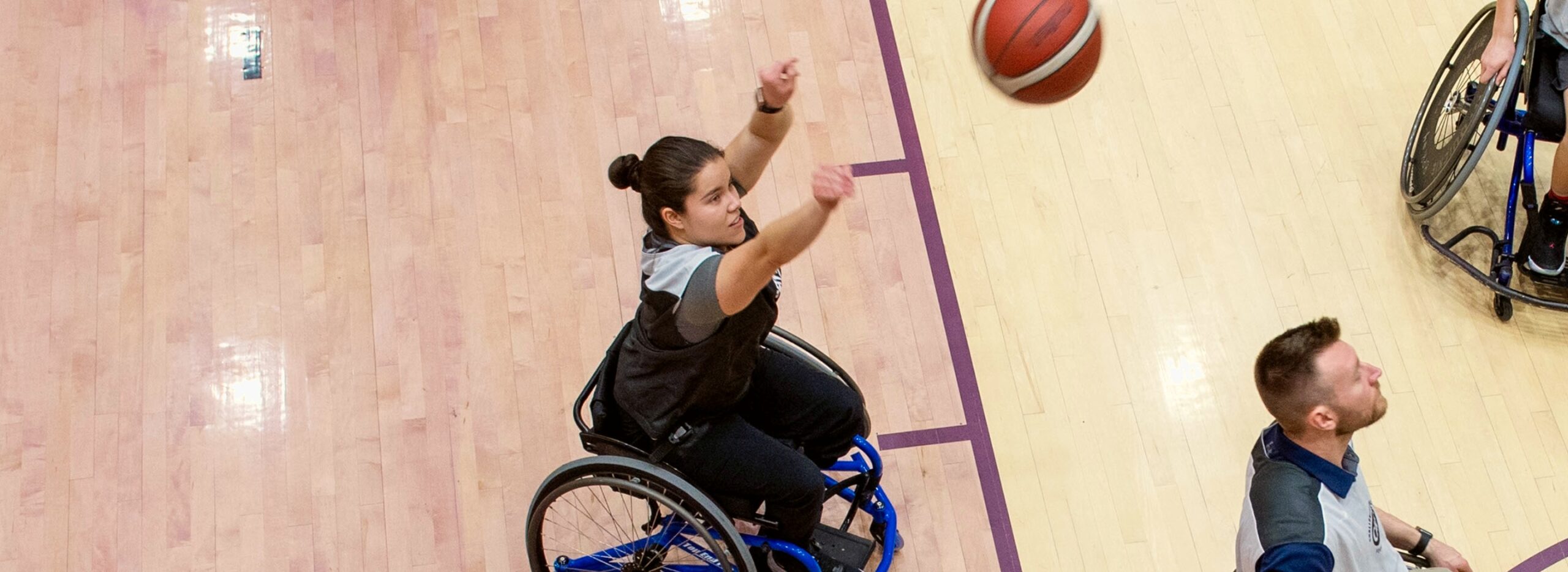 A person in a wheelchair throwing a basketball, with two other people in wheelchairs nearby