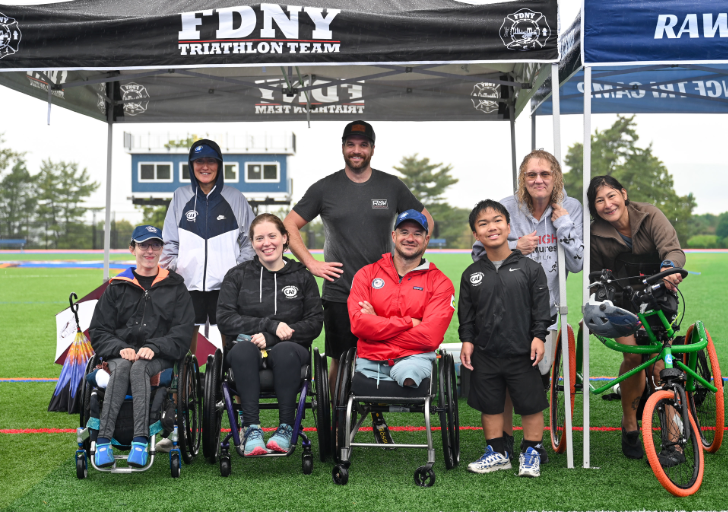 CAF athletes and clinic participants, including wheelchair users and an adaptive cyclist, gather on an outdoor track during the CAF Northeast Paratriathlon Clinic.
