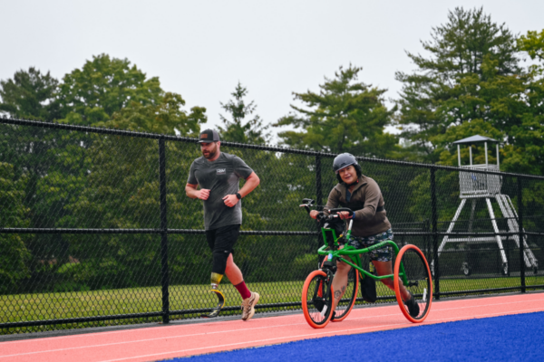 A CAF athlete runs on an outdoor track in rainy conditions during the CAF Northeast Paratriathlon Clinic.
