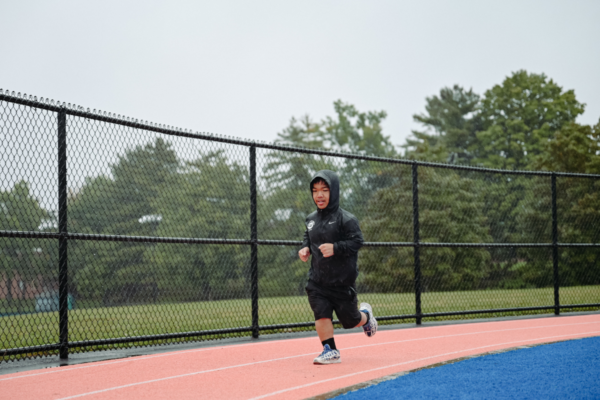 A CAF athlete runs on an outdoor track in rainy conditions during the CAF Northeast Paratriathlon Clinic.