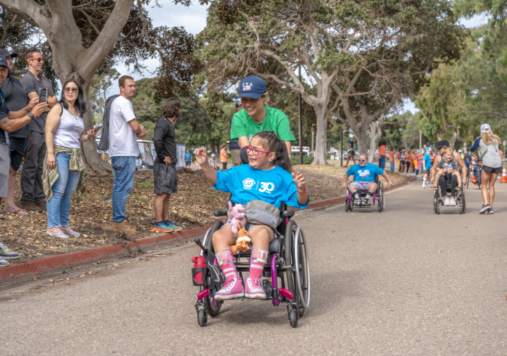 Young athlete is pushed in a racing wheelchair during a Challenged Athletes Foundation kids event focused on inclusion and adaptive sports.