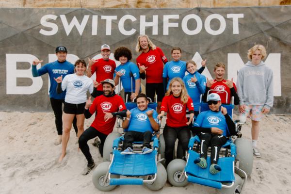 Youth participant stands with family members while holding a CAF-branded surfboard at an adaptive surfing event.